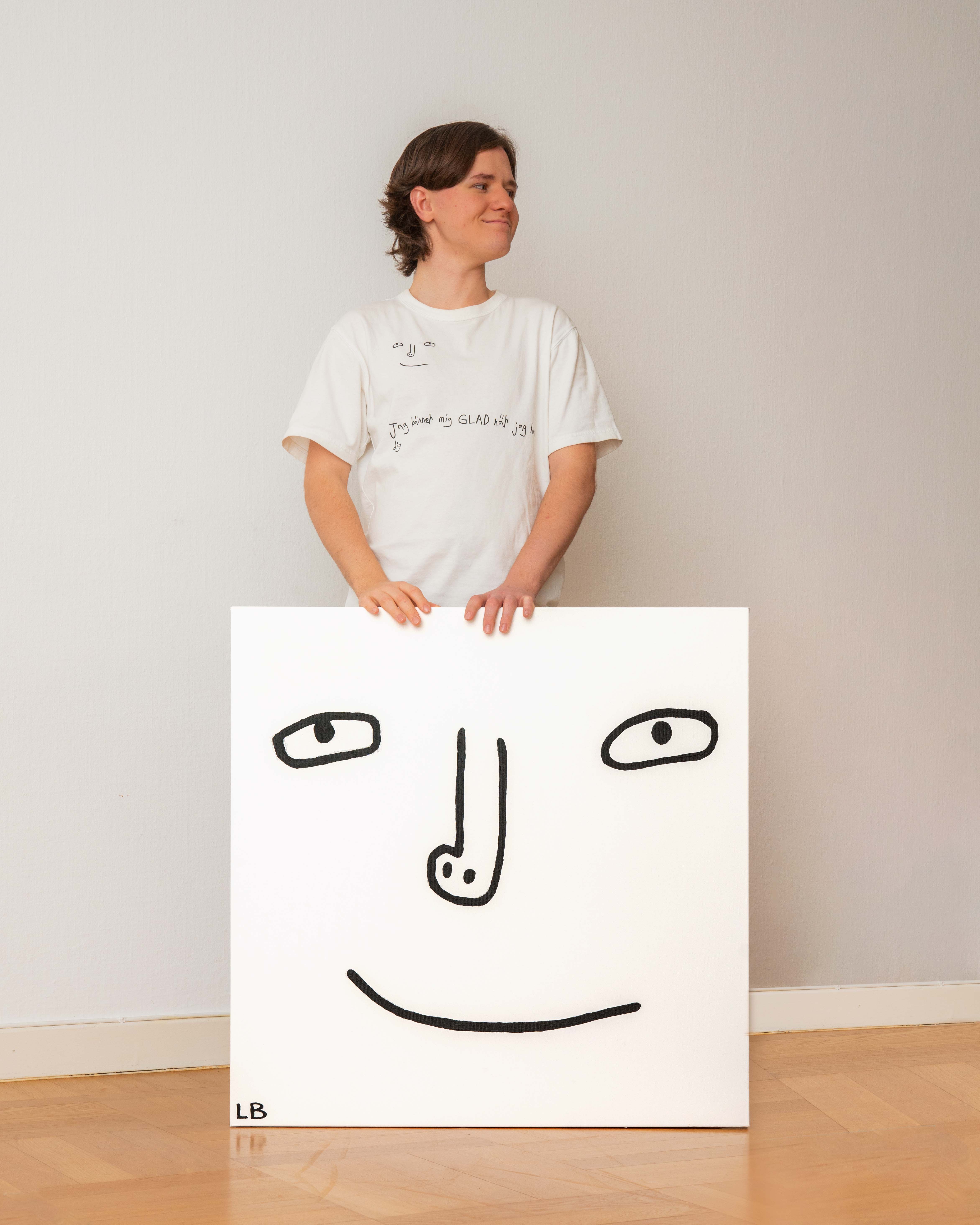 Ludde står med en stor canvas med sitt ritade ansikte på