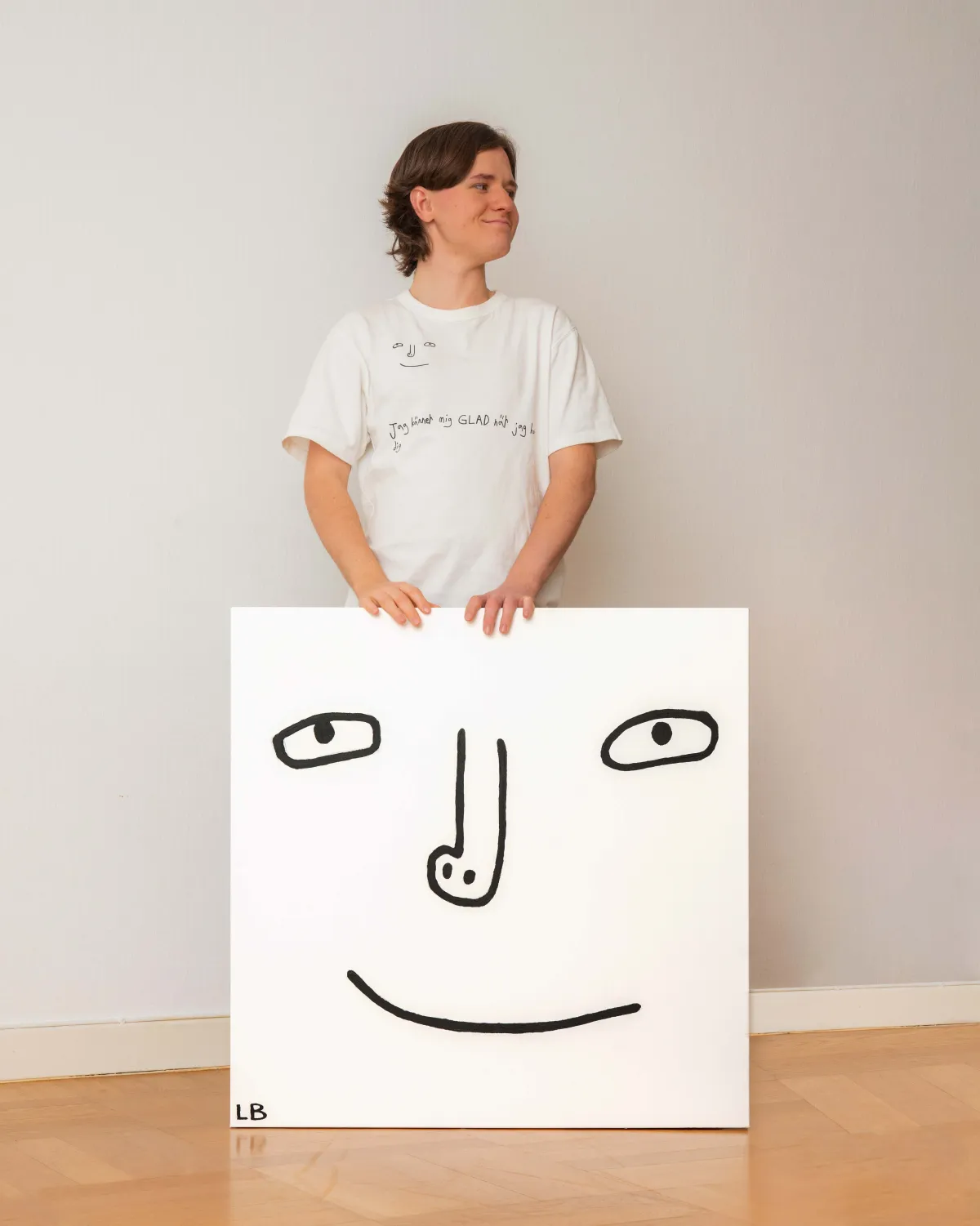 Ludde står med en stor canvas med sitt ritade ansikte på